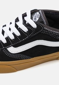 Pantofii de skateboard din suede negru, cu o bandă laterală albă, șireturi albe și accente cusute. Talpa din cauciuc are un model texturat pentru aderență.