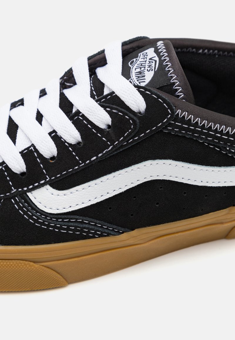 Zapatilla de skate de ante negro con franja lateral blanca, cordones blancos y detalles cosidos. La suela de goma presenta un patrón texturizado para mayor agarre.