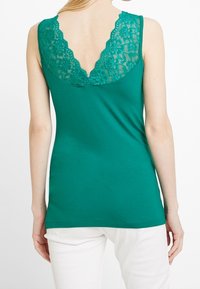 Top sin mangas en color teal con un espalda en forma de V que presenta un acabado de encaje floral. Hecho de una tela suave, tiene un diseño ajustado y tirantes delgados.