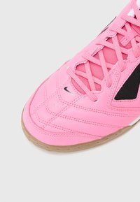 Chaussure de sport rose avec lacets, panneaux en mesh noir, petit logo Nike noir près des orteils et semelle marron clair sur fond gris.