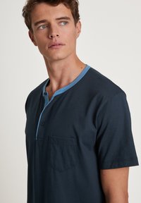 Marineblauwe henley-t-shirt met korte mouwen van zachte stof, met een lichtblauwe kraag, vooraan knopen en een borstzak met een vierkante flap.