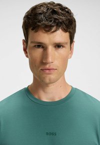 Teal crew-neck T-shirt made of smooth fabric, featuring a subtle embossed "BOSS" logo on the chest. Minimalist design with a fitted shape.
