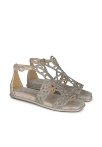 Platte sandalen met een metallic zilveren afwerking, voorzien van een ingewikkeld uitsnijdend ontwerp, een enkelbandje en een zachte, gladde voetbed.