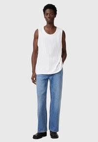 Weißes, geripptes, ärmelloses Top, kombiniert mit hellblauen, weit geschnittenen Jeans und schwarzen Schuhen. Der Stoff wirkt weich mit einer texturierten Oberfläche.