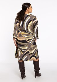 Langärmliges Kleid mit einem mehrfarbigen Spiraldesign in Erdtönen. Es verfügt über ein fließendes Design und einen weichen, dehnbaren Stoff. Knielang.