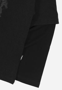 Svart t-skjorte lagt over en annen svart t-skjorte, med en glatt tekstur og et subtilt grafisk design på det øverste laget.