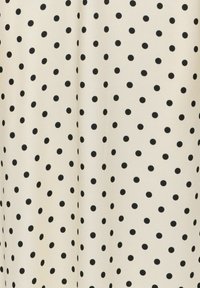 Tissu crème avec un motif irrégulier de petits pois noirs uniformément espacés.