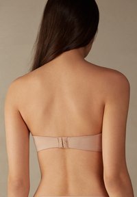 Sujetador sin tirantes beige con tela suave, que cuenta con un cierre de gancho y ojo en la parte posterior y un diseño sin costuras para una silueta limpia.