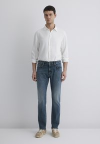 White button-up shirt, blue denim jeans, beige sneakers. Regular fit, straight leg, soft texture, minimal design. Neutral colors, casual look.