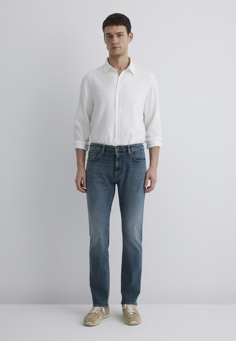White button-up shirt, blue denim jeans, beige sneakers. Regular fit, straight leg, soft texture, minimal design. Neutral colors, casual look.
