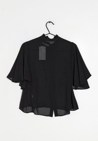 Blusa nera con maniche corte a campana, tessuto texturizzato caratterizzato da un motivo geometrico, scollatura rotonda e orlo posteriore leggermente più lungo.