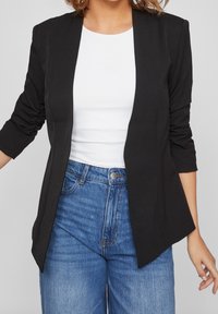 Svart, skräddarsydd blazer med en jämn yta, öppen front och trekvartsärmar, kombinerad med en vit topp och högmidjade blå jeans.