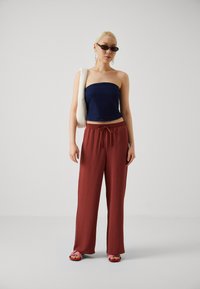Navy strapless top with a fitted design; loose, rust-colored pleated pants; pink and brown slip-on sandals; white shoulder bag; dark sunglasses.