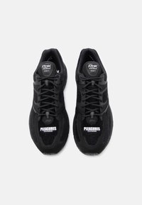 Črne športne čevlje z teksturiranim zgornjim delom, ki imajo črne vezalke, blagovno znamko na jezikih in drage bele napise "PLEASURES DMX RIDE" na strani.