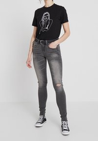 Svart t-shirt med vit linjeteckning, kombinerad med grå skinny jeans med ripped detaljer, och svarta sneakers.