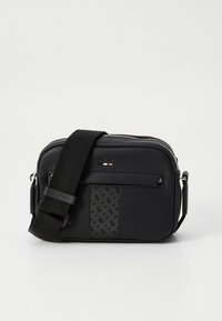 Černá kabelka přes tělo s nastavitelným řemínkem, přední kapsou na zip, texturovaným panelem a malým raženým logem na hladkém materiálu.