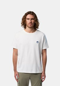 T-shirt bianco in cotone con colletto rotondo e maniche corte, con un piccolo logo circolare blu sul lato sinistro del petto.