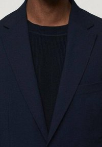 Granatowa marynarka z klapami, pojedyncza kieszeń na piersi, dopasowany fason, noszona na ciemnym, teksturowanym swetrze.