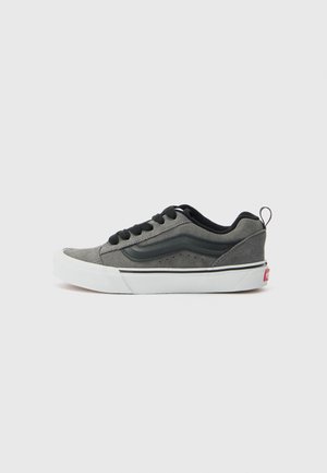 Tenis gri din suede cu accente negre, șireturi plata, talpă din cauciuc alb și dunga semnătură pe lateral. Vârf rotunjit și tab de călcâi mic.