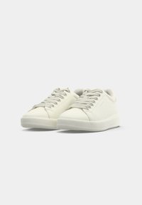 Sneakers bianche in pelle con punta rotonda, suola piatta in gomma e lacci tonali, caratterizzate da una texture liscia e da un design minimalista.