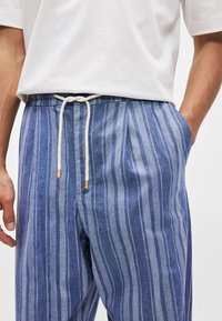Μπλε και λευκές ριγέ λινές παντελόνες με ελαστική μέση, με υφή υφάσματος και διακριτική γυαλάδα, σχεδιασμένες για άνεση και αναπνοή.