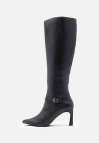 Stivale nero al ginocchio in pelle, con punta affusolata, tacco a stiletto e un cinturino decorativo alla caviglia con una fibbia dorata.