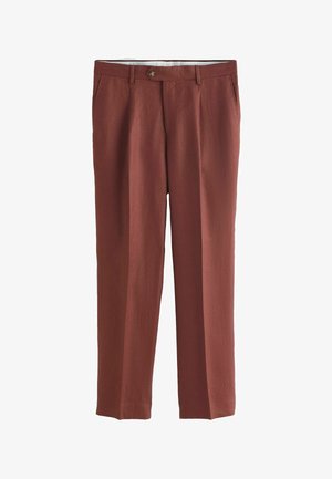 Mężczyzna w rdzawych spodniach z bocznymi kieszeniami oraz beżowej krótko rękawowej dzianinowej koszuli z pionowymi paskami i guzikami.