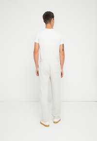 Pantalones de chándal grises con un corte relajado, que cuentan con una cinturilla elástica y un bolsillo trasero, combinados con una camiseta blanca básica y zapatos beige.