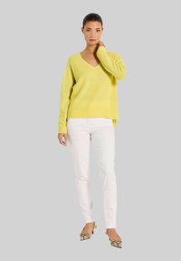 Gelber V-Ausschnitt-Pullover aus weichem Strickstoff, kombiniert mit weißen, schmal geschnittenen Jeans und Schuhen mit Schlangenledermuster. Einfaches Design, lockere Passform.