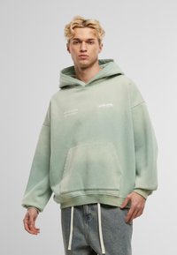 Sudadera de algodón verde menta con un bolsillo frontal, cordones y logotipo en texto blanco. Presenta un diseño oversize y puños acanalados.