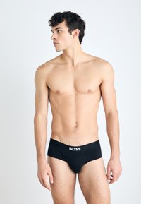 Schwarze Baumwollslips mit einem weißen "BOSS"-Logo am Bund, mit einem eng anliegenden Design und glatter Textur, präsentiert auf einem Torso.