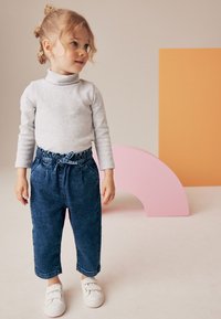 Bambino che indossa un dolcevita grigio chiaro e pantaloni di jeans blu con vita elastica, abbinati a sneaker bianche con velcro.