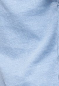 Tissu en coton bleu clair avec des coutures visibles et des plis doux créant texture et ombres.