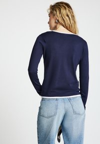 Marineblaues Langarmoberteil mit rundem Ausschnitt, kombiniert mit hellblauen, hoch taillierten Jeans. Der Stoff wirkt weich und eng anliegend.