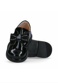 Scarpe in pelle verniciata nera con un ampio fiocco e accenti di borchie, punta tonda e suola piatta in gomma. L'interno è beige.