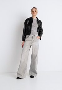 Μαύρο κοντό δερμάτινο μπουφάν, ριγέ μακρυμάνικη μπλούζα και γκρι τζιν με φαρδιά μπάρα. Μαύρα παπούτσια. Απλός σχεδιασμός, ομαλή υφή και διακριτικά χρώματα.