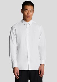 Camicia bianca a maniche lunghe con bottoni, caratterizzata da un colletto a punta, un logo ricamato sul petto e una morbida texture in cotone.