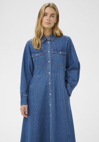 Denim jurk met een kraag, lange mouwen, twee borstzakken, knoopsluiting aan de voorkant en een losse, vloeiende pasvorm in een blauwe tint.