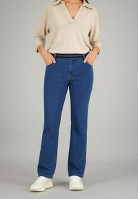 Jeans in denim blu con taglio dritto, vita alta e dettagli di cucitura sottili, abbinati a un maglione beige e sneakers bianche.