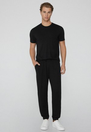 Black short-sleeve t-shirt and black drawstring pants. Smooth fabric, standard fit, elastic cuffs on pants, paired with white sneakers.