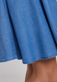 Blå denimkjol med en mjuk textur, utställd design och rå kant. Tyget visar en subtil blekning som framhäver dess avslappnade stil.