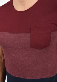 Short-sleeve T-shirt featuring a color-block design with maroon and dark blue sections and a small chest pocket in matching maroon fabric.