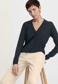 Cardigan léger bleu marine avec un décolleté en V, des manches longues et six boutons sur le devant, associé à un pantalon de couleur claire.