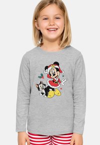 Bambino sorridente con una maglietta a maniche lunghe grigia con Minnie Mouse in abbigliamento da Babbo Natale e grafica di un gatto nero, che indossa pantaloni a righe rosse e bianche.