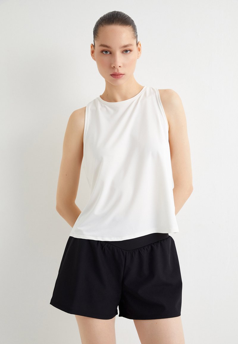 Top blanco sin mangas con una textura suave, combinado con pantalones cortos negros con cinturilla elástica, ambos en ajuste relajado.