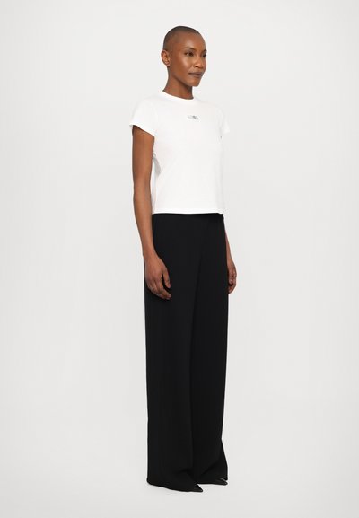 White, short-sleeve T-shirt with a cropped design and small black logo, paired with loose-fitting black trousers. Smooth fabric texture.