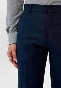 Marineblauwe broek van glad materiaal, met een vlakke voorkant, zakken aan de zijkant en een getailleerde pasvorm, gecombineerd met een lichtgrijs T-shirt met lange mouwen.