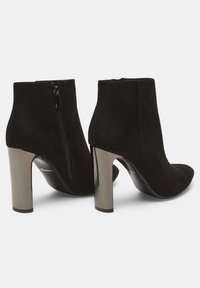 Stivaletti in suede nera alla caviglia con punta appuntita e zip laterale. Presentano un tacco a blocco metallico per maggiore altezza e stabilità.