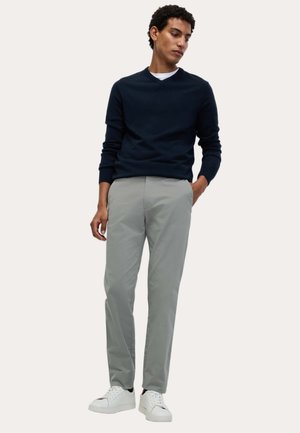 Suéter de punto azul marino, pantalones grises claros y zapatillas blancas. El conjunto presenta un corte clásico con líneas simples y acentos mínimos.