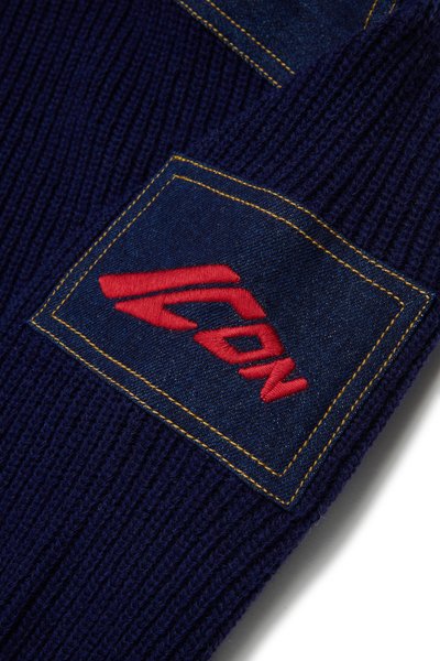 Bonnet tricoté bleu marine avec un patch en denim, des coutures jaunes et un logo brodé rouge. Texture côtelée avec un design structuré.